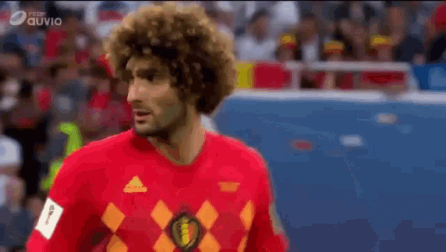 a man with curly hair wearing a red adidas shirt