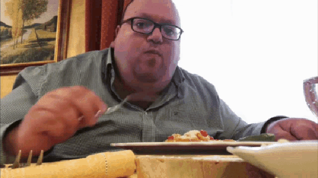 a man with glasses is sitting at a table eating food