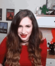 a woman wearing a red shirt and red lipstick is sitting in front of a cactus .