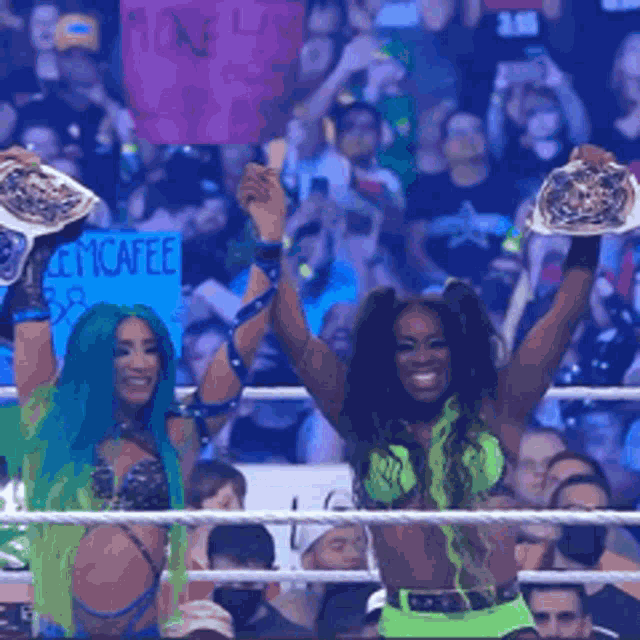 two women in a wrestling ring holding up trophies in front of a crowd with a sign that says emcafee in the background