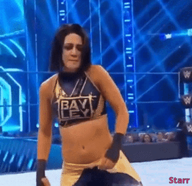 a female wrestler wearing a top that says bay is dancing on a stage .