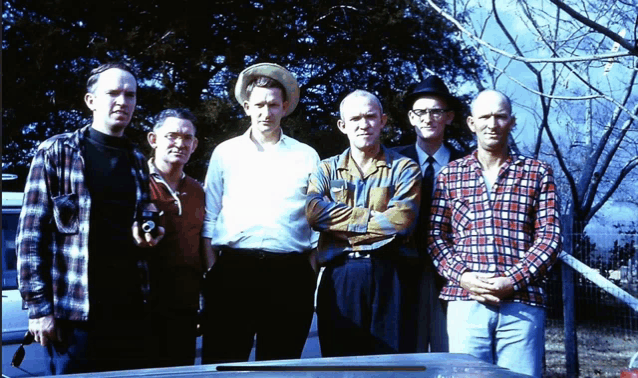 a group of men are posing for a picture with a car in the background