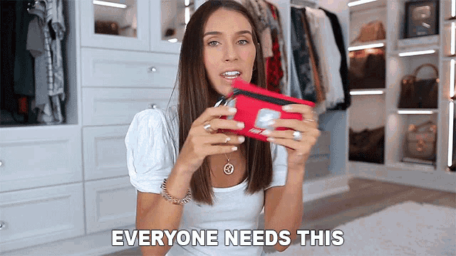 a woman in a white shirt is holding a red wallet and the words everyone needs this are above her