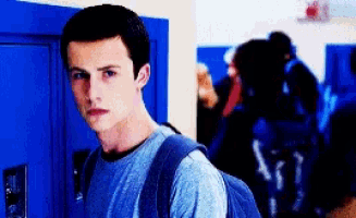 a boy with a backpack is standing in front of a blue locker .