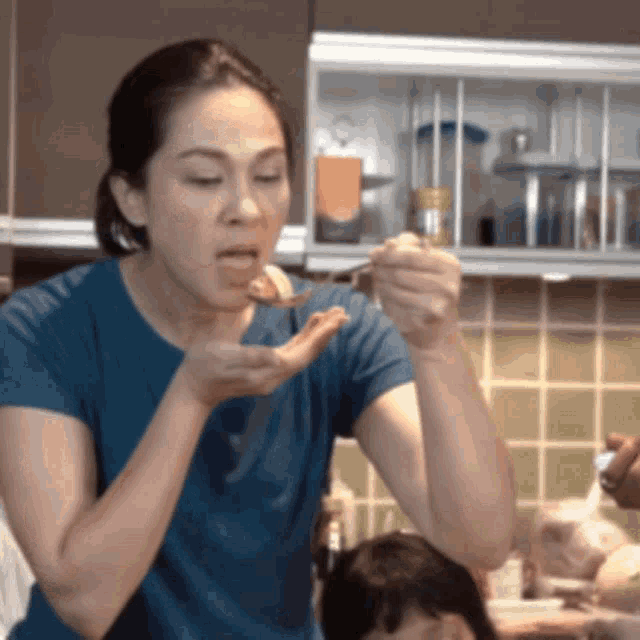 a woman in a blue shirt is eating something with a spoon in her hand