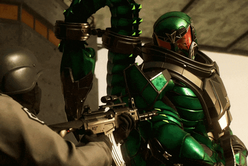 a man in a green suit is holding a gun in front of another man in a black helmet