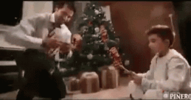 a man and a boy are playing with a toy in front of a christmas tree .