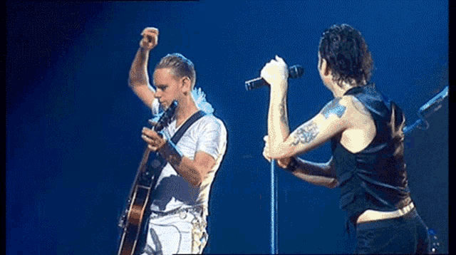 a man singing into a microphone while another man holds a guitar