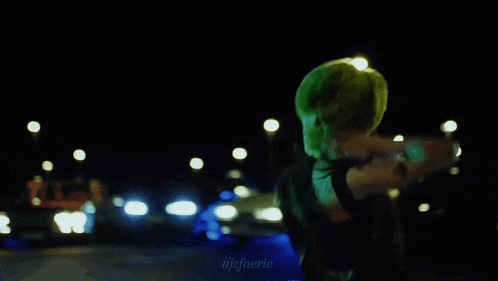 a woman in a green hat is standing in front of a car at night with njfaene written on the bottom right