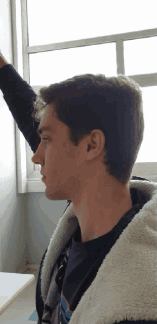 a young man in a black shirt and a white jacket looks out a window