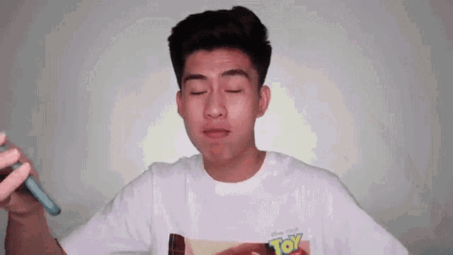 a young man wearing a toy story t-shirt is eating a chocolate bar with his eyes closed .