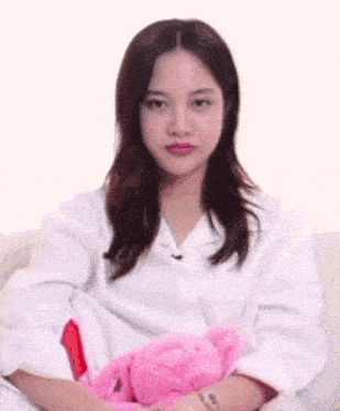 a woman in a white shirt is sitting on a couch holding a pink teddy bear .