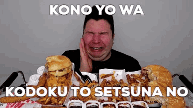 a man is sitting at a table with hamburgers and french fries and says kono yo wa ko doku to setsuna no