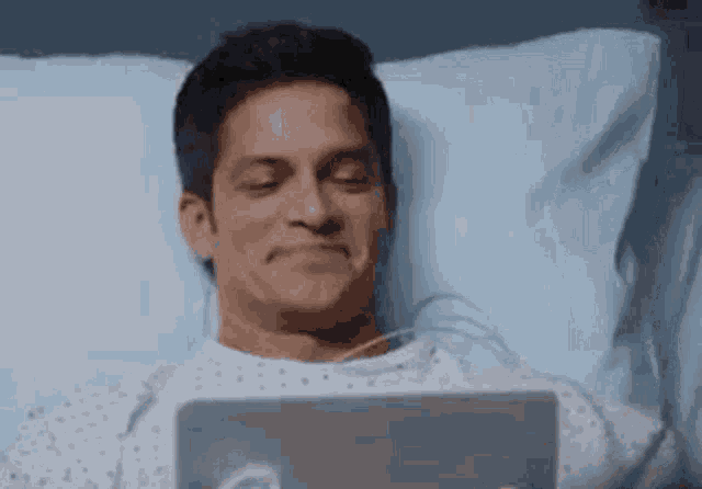 a man is laying in a hospital bed using a tablet .