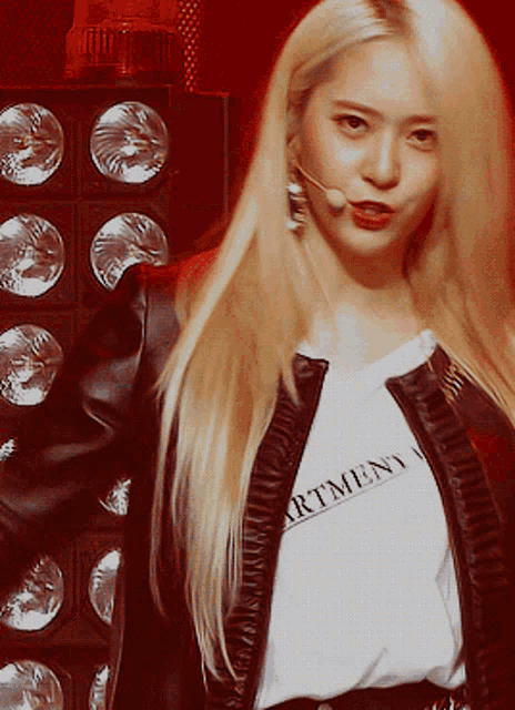 a blonde woman wearing a black jacket and a white shirt that says " artment "