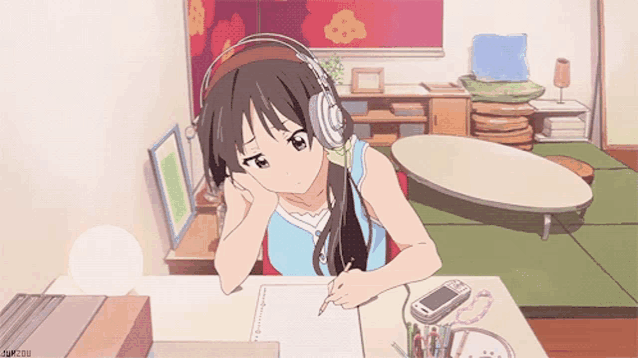 a girl wearing headphones sits at a desk writing