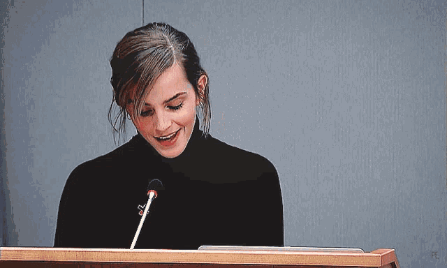 a woman stands at a podium with a microphone in front of her