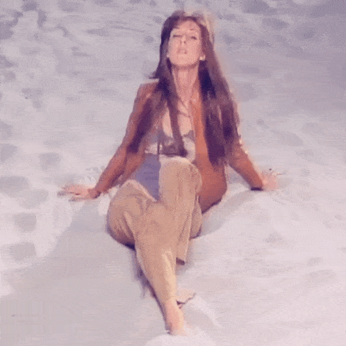 a woman sitting on a sandy surface with her legs crossed