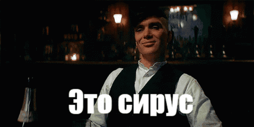 a man in a white shirt and black vest says " это сирус " in a dark room