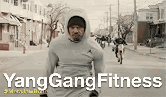 a man wearing a hoodie is running down a street with the words yang gang fitness written on the bottom