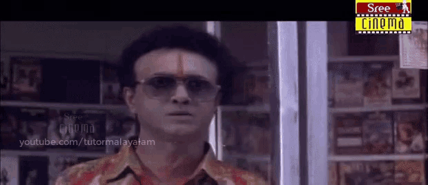 a man wearing sunglasses and a hat is standing in front of a shelf with a sign that says sree cinema