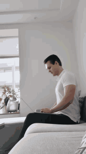 a man in a white shirt is sitting on a couch using a laptop