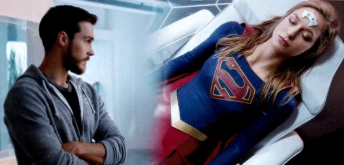a man is standing next to a woman in a superman costume laying on a bed .