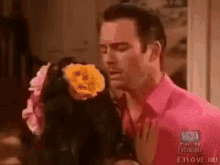 a man in a pink shirt is holding a doll with a face on it 's head .