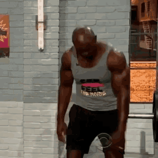 a man wearing a grey tank top that says " feel the noise " is lifting a barbell