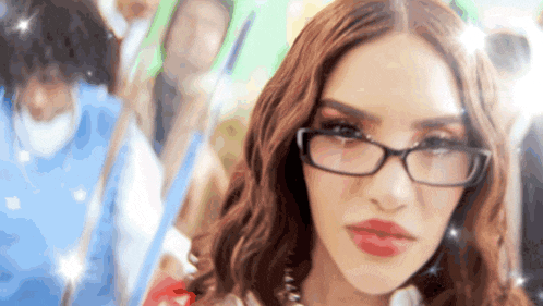 a woman wearing glasses and red lipstick is standing in front of a crowd .
