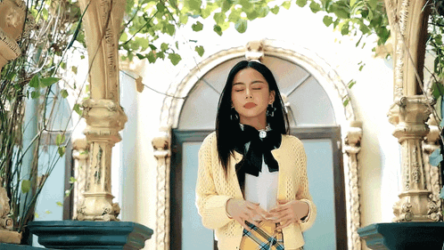 a woman in a yellow sweater and plaid skirt is standing in front of a building holding a piece of paper .