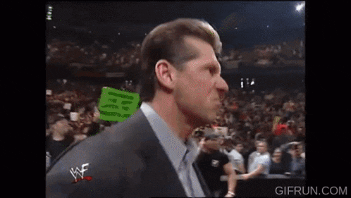 a man in a suit and tie is standing in front of a crowd with a sign that says wwe on it .
