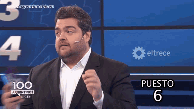 a man in a suit is standing in front of a screen that says puesto 6