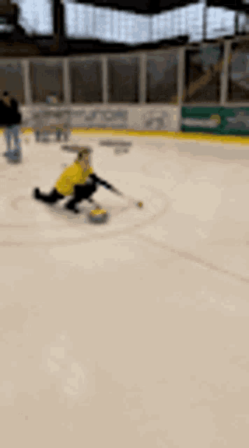 a person in a yellow shirt is playing curling on an ice rink .
