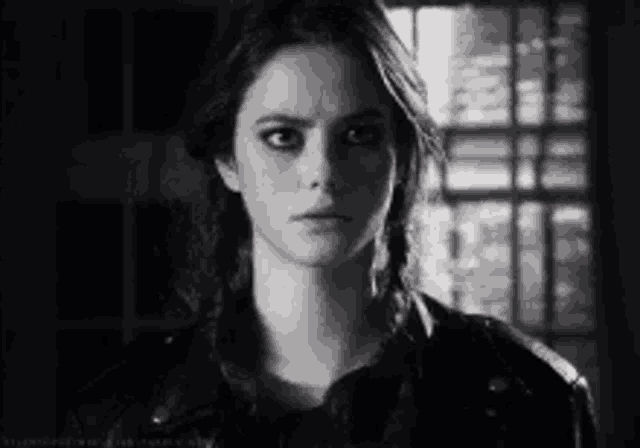 a black and white photo of a woman wearing a leather jacket and looking at the camera .