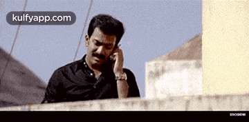 a man is talking on a cell phone while sitting on a ledge .