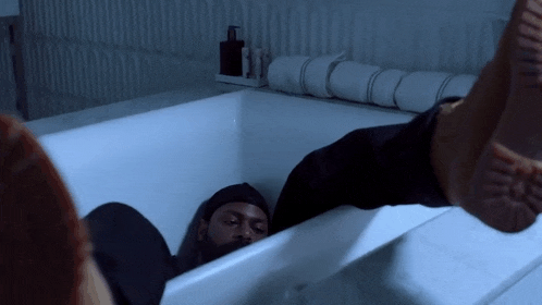 a man is laying in a bathtub with his feet up and his head down .