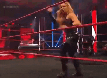 a wrestler is standing in the middle of a wrestling ring holding a barbell .