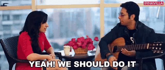 a man playing a guitar next to a woman who is sitting at a table