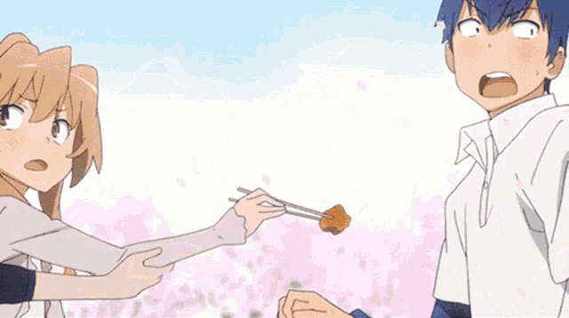 a boy and a girl are standing next to each other and the girl is holding a piece of meat with chopsticks
