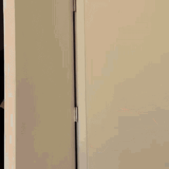 a woman in a black dress is peeking out from behind a white door