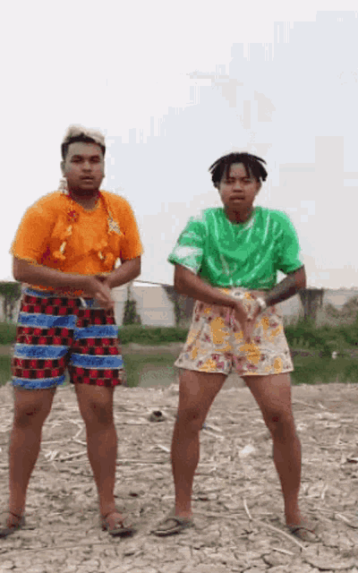 a couple of men are standing on a dirt field .