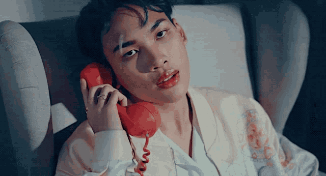 a man is laying in a chair talking on a red telephone