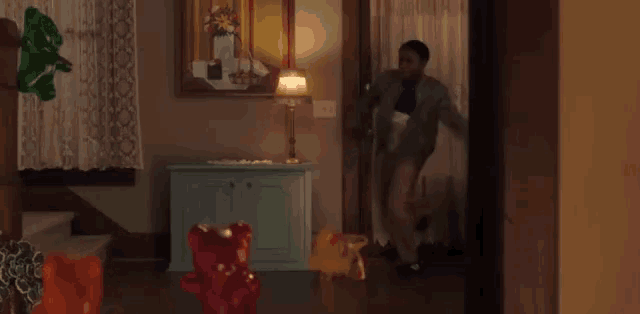 a man is standing in a living room next to a lamp and a dresser .
