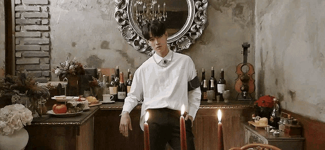 a man in a white shirt stands in front of a mirror holding candles