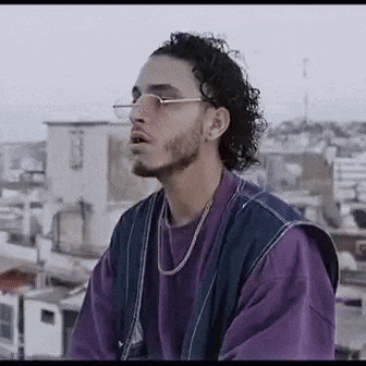 a man with curly hair and a beard wearing glasses and a purple shirt is standing on a rooftop .