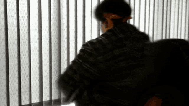 a person standing in front of a window with blinds