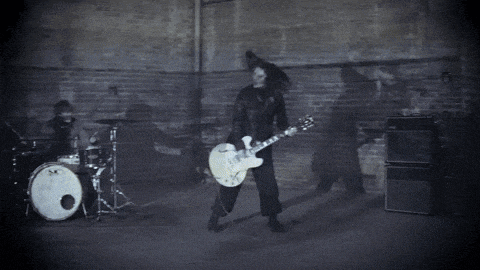 a man in a gas mask is playing a guitar in a dark room