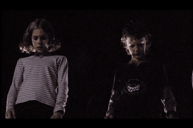 a girl in a striped shirt is holding a boy 's hand in the dark