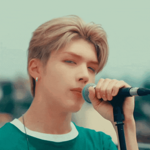 a young man singing into a microphone in a green shirt